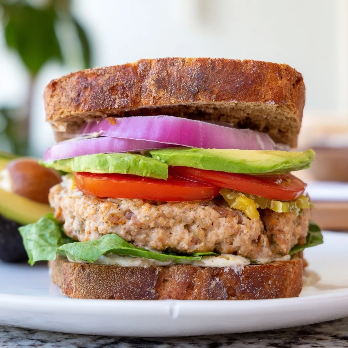 A juicy turkey burger with avocado on a toasted whole wheat bun, garnished with fresh parsley and crisp red onion slices.