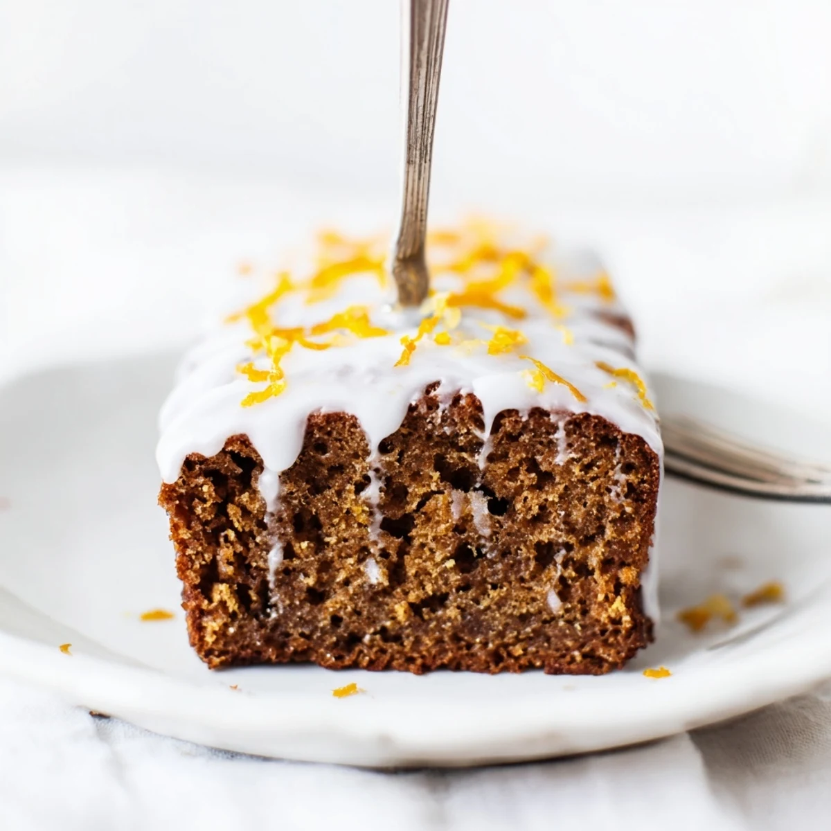 Freshly baked Gingerbread Loaf with Orange Icing on a wooden cutting board, drizzled with sweet glaze and ready to slice.