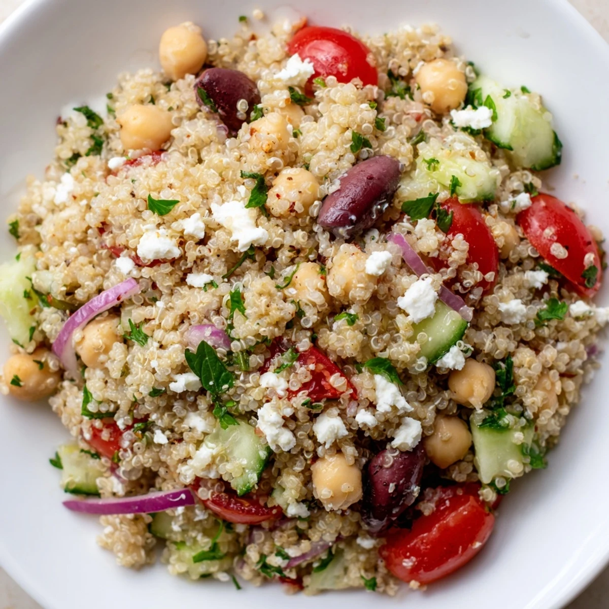 Tossed Mediterranean Quinoa Salad featuring chickpeas, crisp cucumber, and Kalamata olives drizzled with zesty lemon-herb dressing.