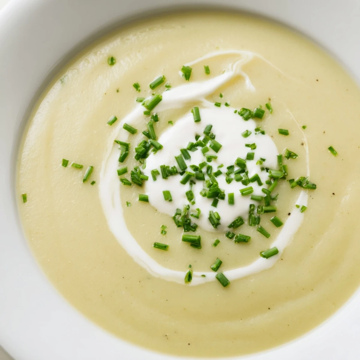 A spoon lifting creamy blended Potato Leek Soup with Chives from a white ceramic bowl, showing smooth, velvety texture.