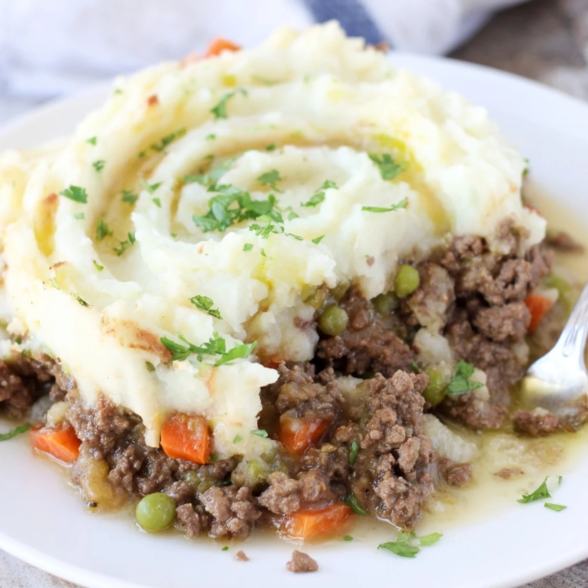 Golden-brown Beef Shepherds Pie with Cauliflower Mash Topping bubbling in a ceramic baking dish, garnished with fresh parsley.