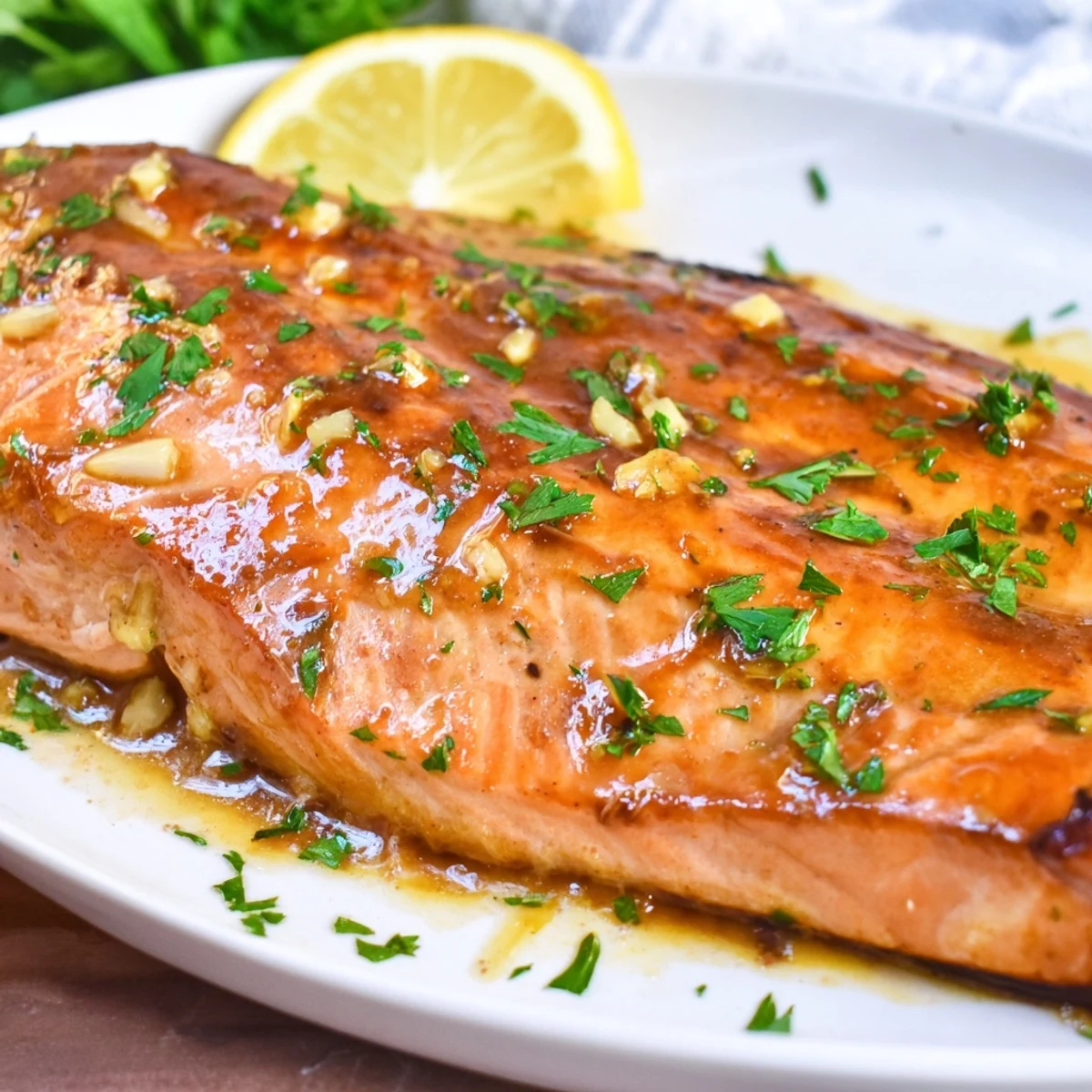 Freshly baked salmon with honey garlic soy glaze resting on a white plate next to colorful roasted vegetables.