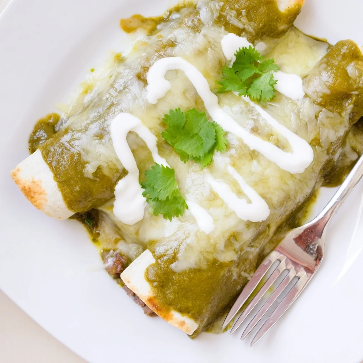 Tender shredded beef filling inside soft corn tortillas, topped with vibrant green sauce and fresh cilantro garnish.