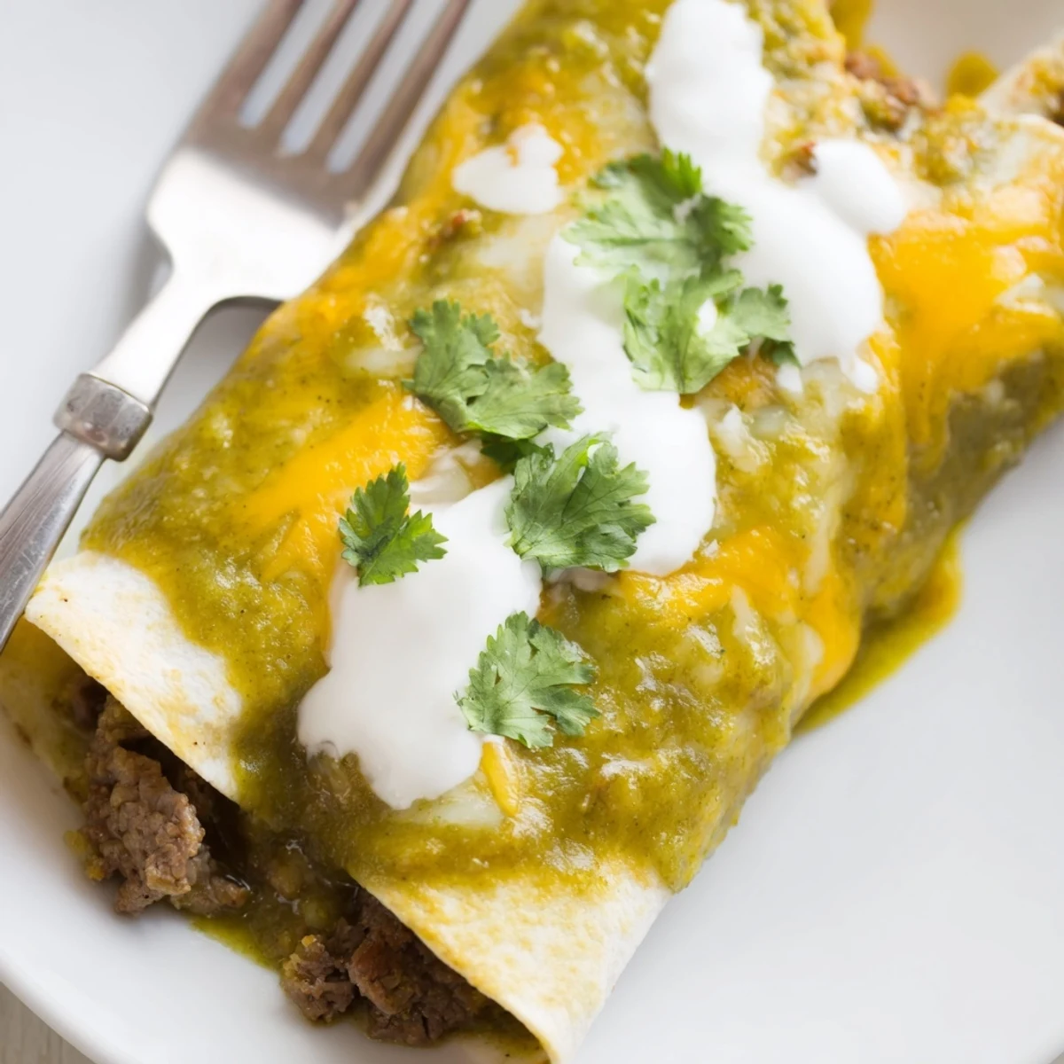 Golden beef enchiladas with green sauce, served hot with sour cream and diced red onion on top.