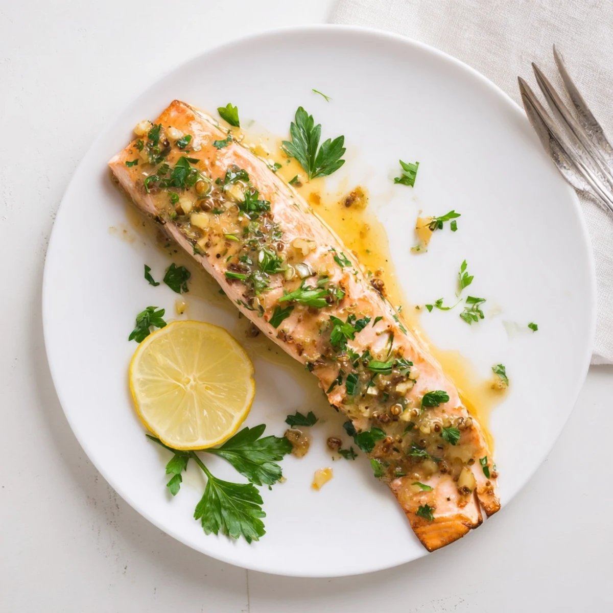 Four golden-baked salmon fillets glazed with a sweet honey mustard sauce, garnished with fresh parsley and lemon wedges on a white plate.