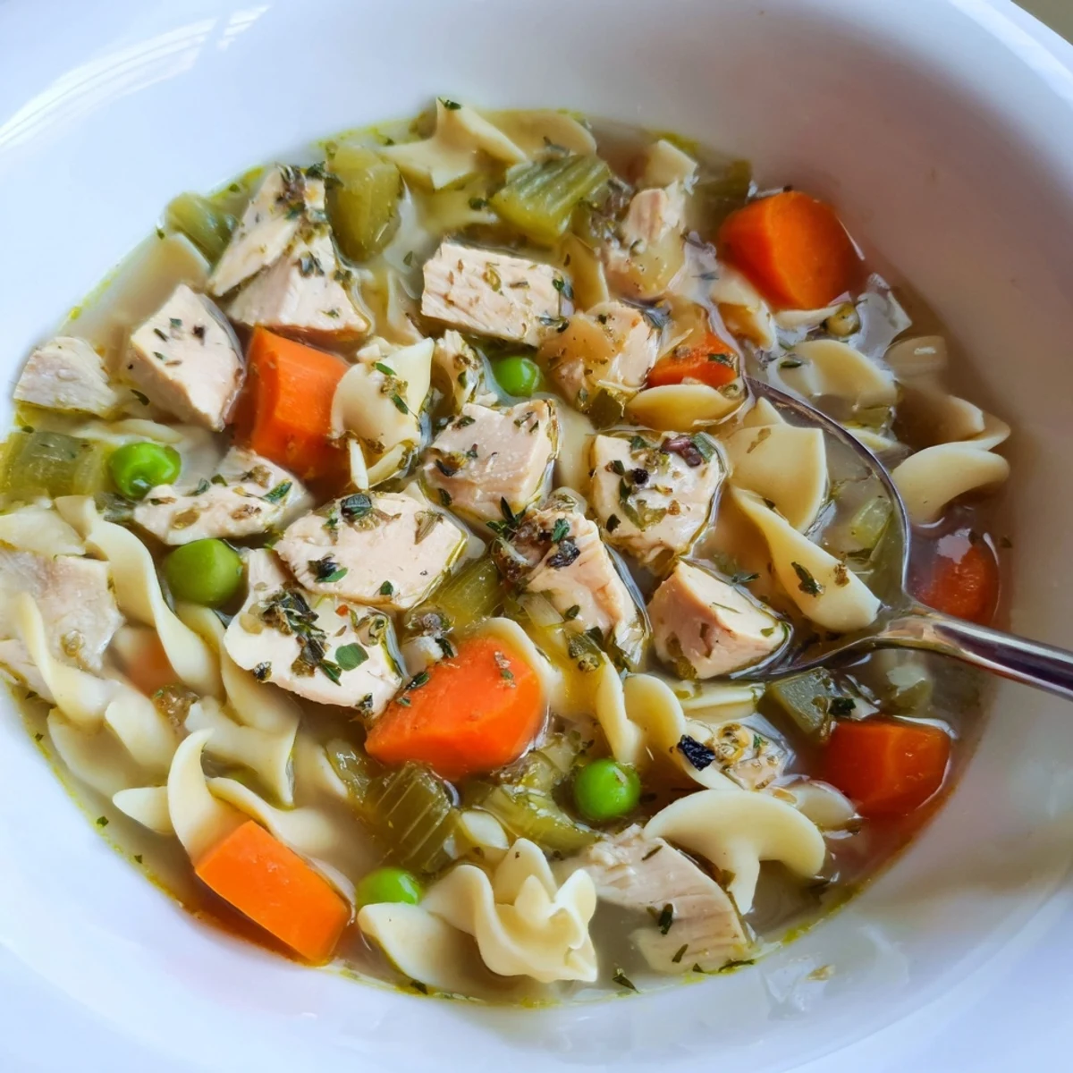 A cozy serving of Chicken Noodle Soup with Veggies sits beside crusty bread, steam rising from the hearty American classic meal.