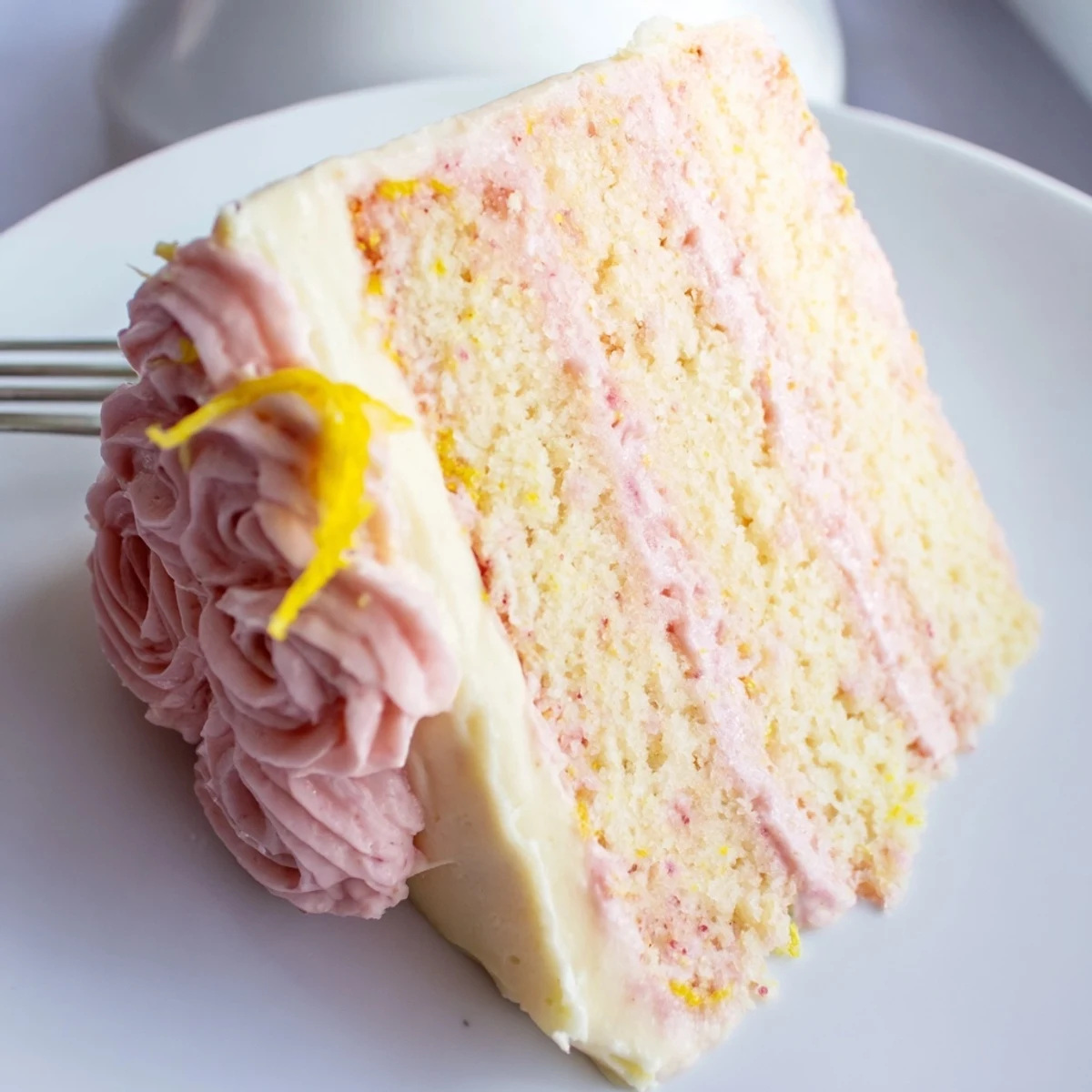 Vibrant Pink Lemonade Layer Cake slices served on a white plate with fresh lemon zest and edible flowers.  