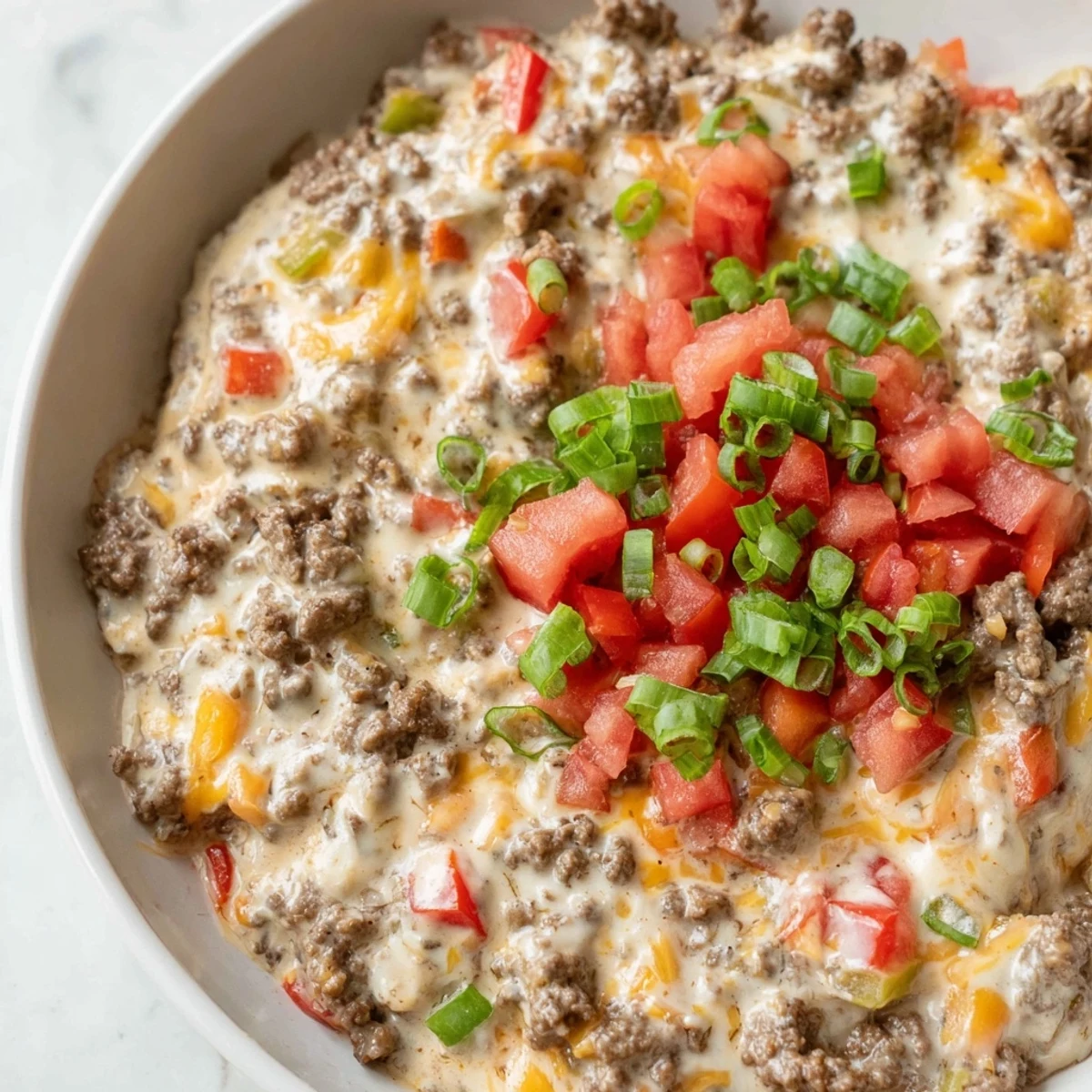 Creamy Queso Dip with Ground Beef and Peppers, garnished with cilantro and tomatoes, served warm with tortilla chips.