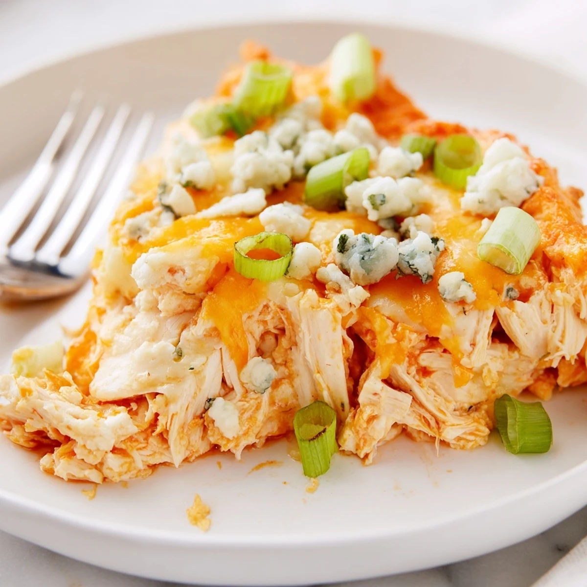 Spicy shredded chicken and creamy cheese dip in a white baking dish, perfect for parties.