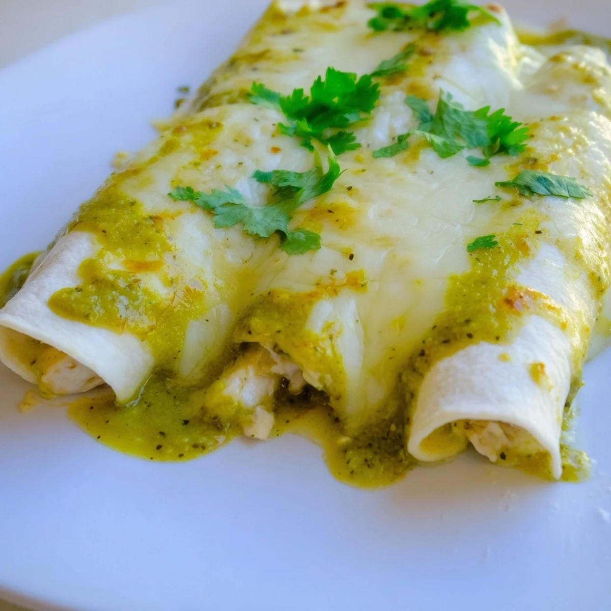 A close-up of Green Enchiladas With Chicken reveals shredded chicken filling in corn tortillas and tangy green sauce.