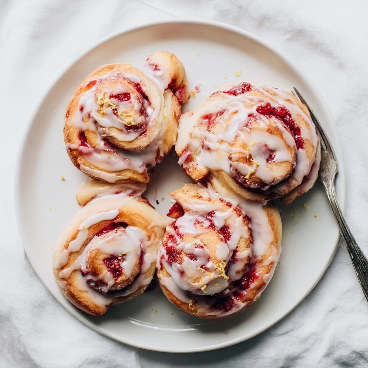 Warm Raspberry Cinnamon Rolls With Lemon Glaze are served on a plate, perfect for a sweet breakfast treat.