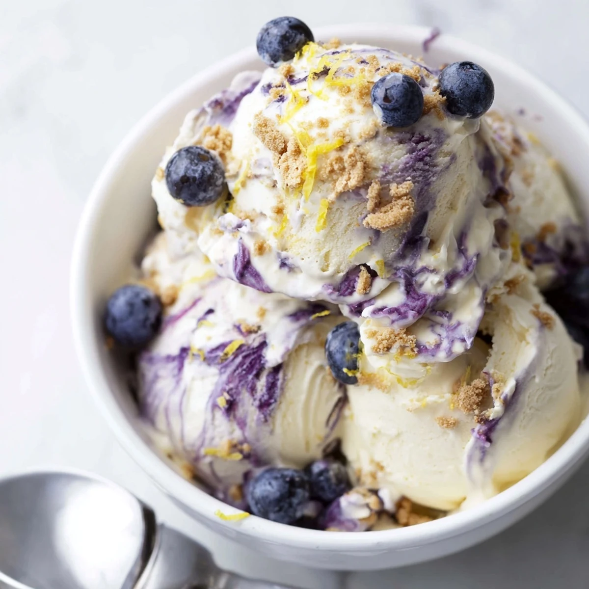 A graham cracker crumb topping adds texture to the Lemon Blueberry Cheesecake Ice Cream served in a glass.