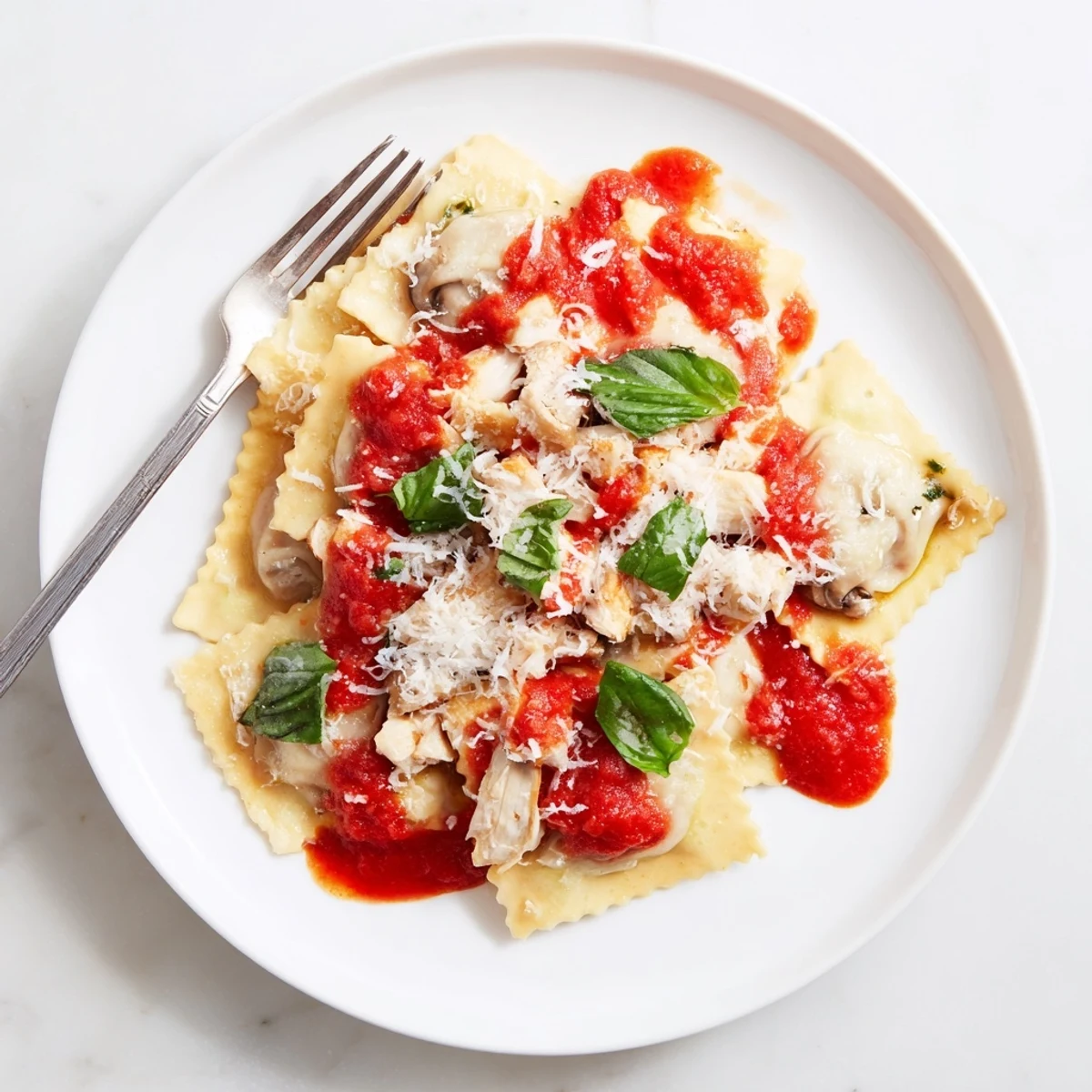 Overhead view of plated Chicken and Mushroom Ravioli with Simple Tomato Sauce, sauce pooling around pasta squares topped with fresh basil.