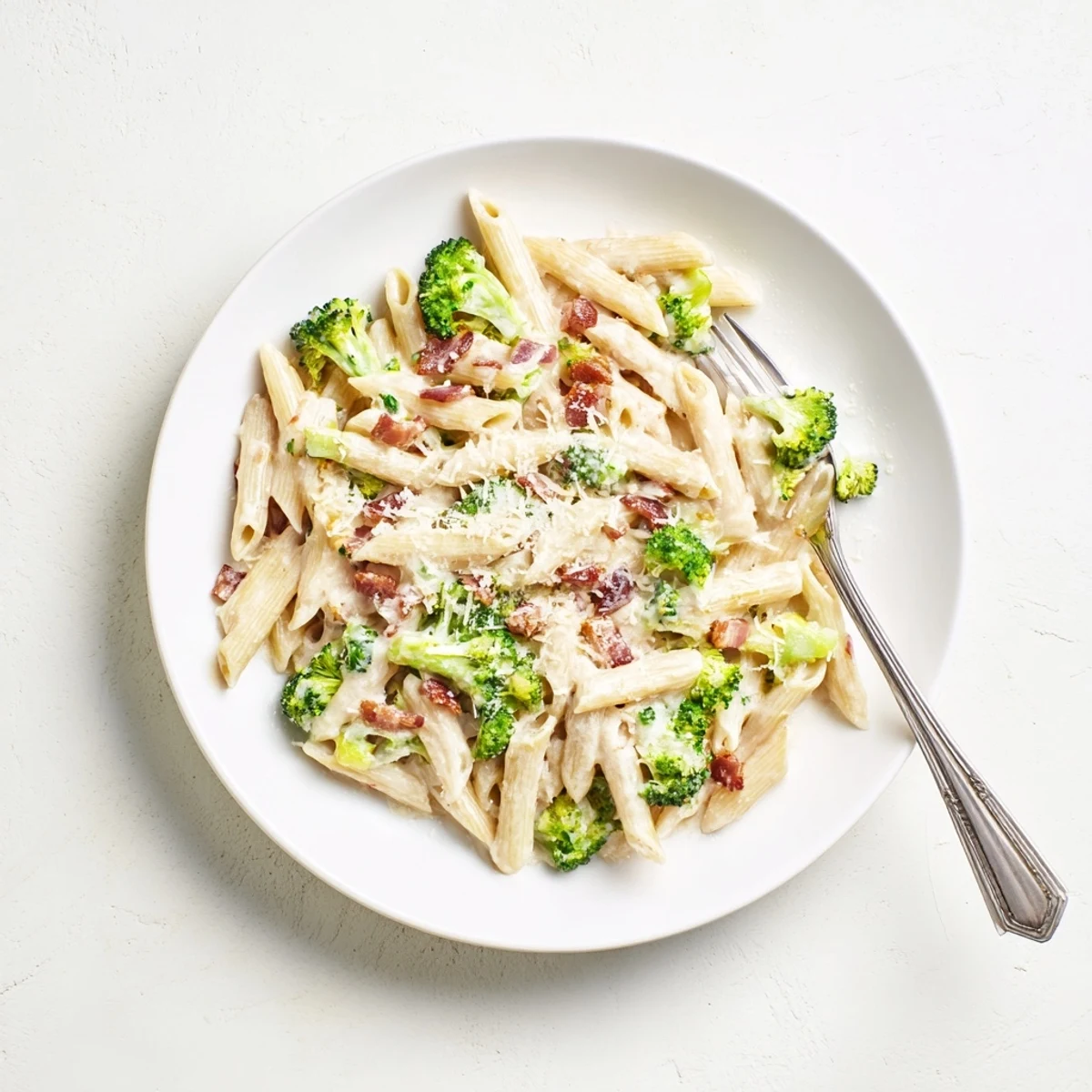 Creamy bacon broccoli and Parmesan pasta in a rustic skillet, garnished with extra cheese and red pepper flakes for serving.