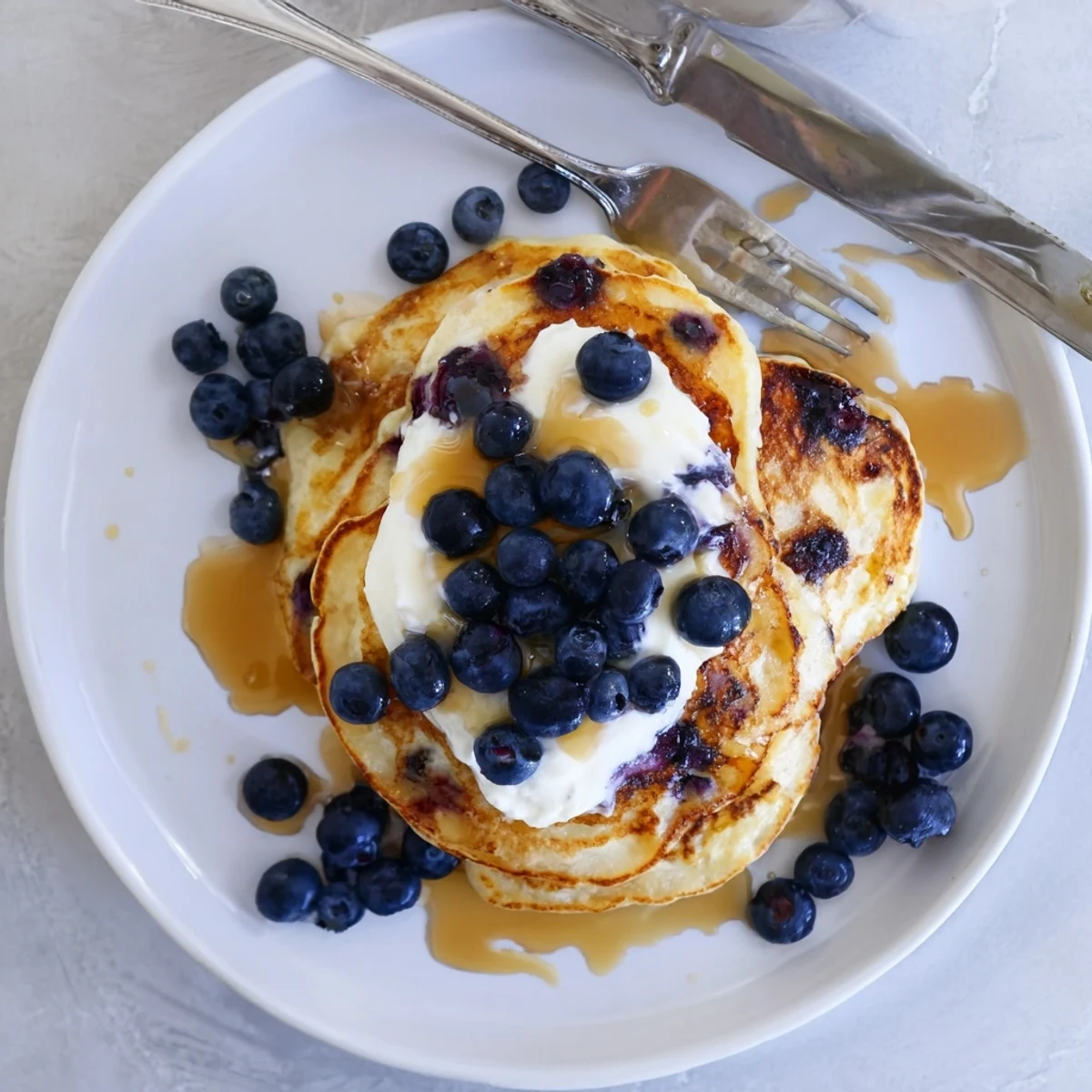 Fluffy Greek Yogurt Blueberry Pancakes stacked high with fresh berries and maple syrup drizzle