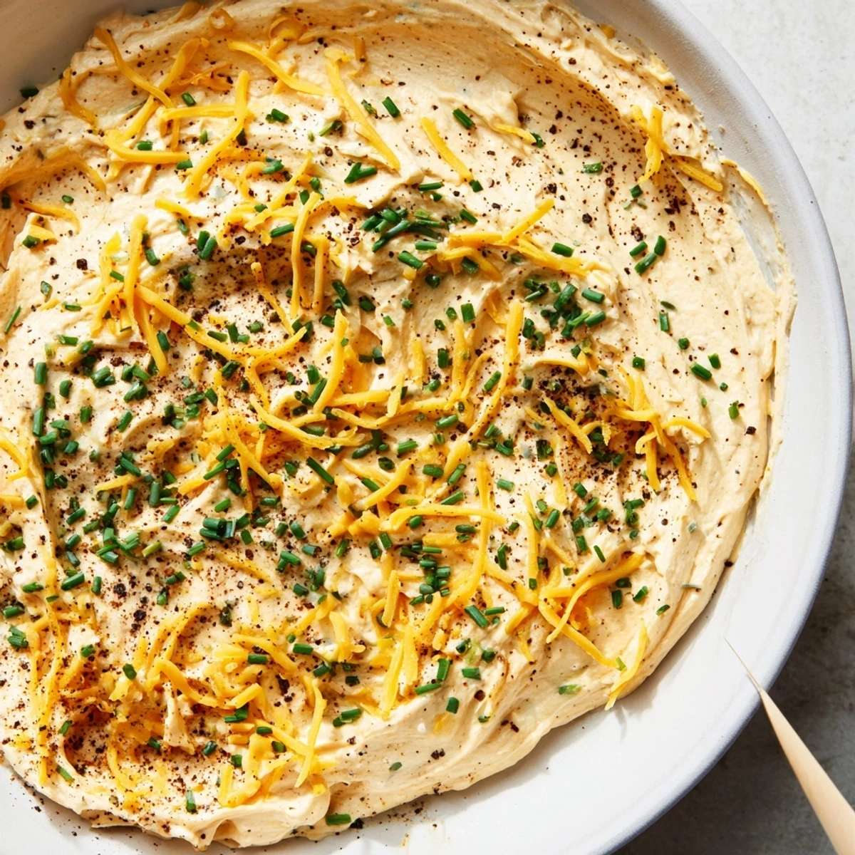 Creamy savory pretzel dip with sharp cheddar and fresh chives served in a white bowl beside warm soft pretzels