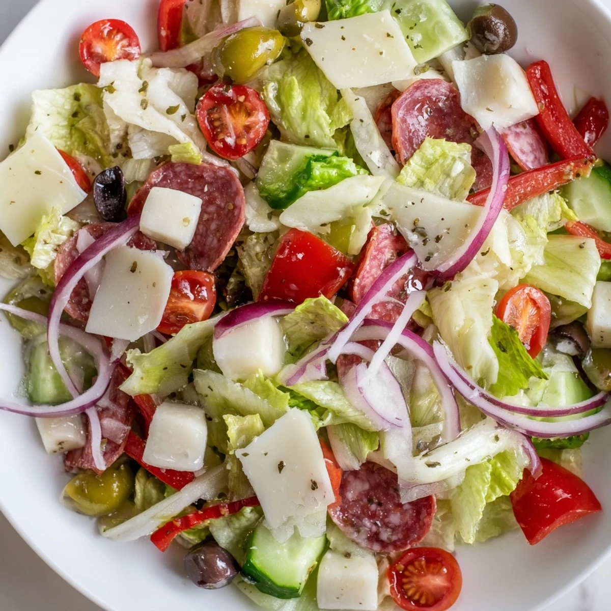 Fresh Italian chopped salad with crisp romaine, salami, olives, and tangy homemade dressing served in a white bowl