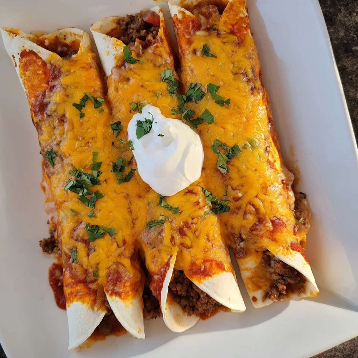 Bubbling pan of savory beef enchiladas topped with melted cheddar and fresh cilantro garnish