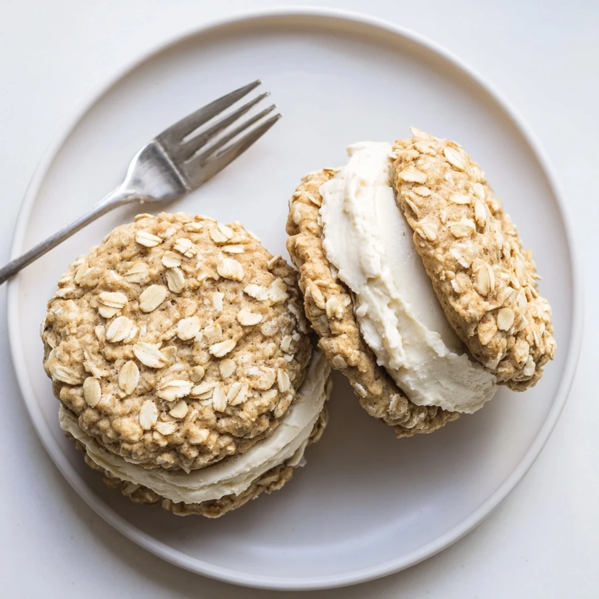 Golden homemade oatmeal cream pies featuring fluffy vanilla frosting sandwiched between soft chewy oatmeal cookies
