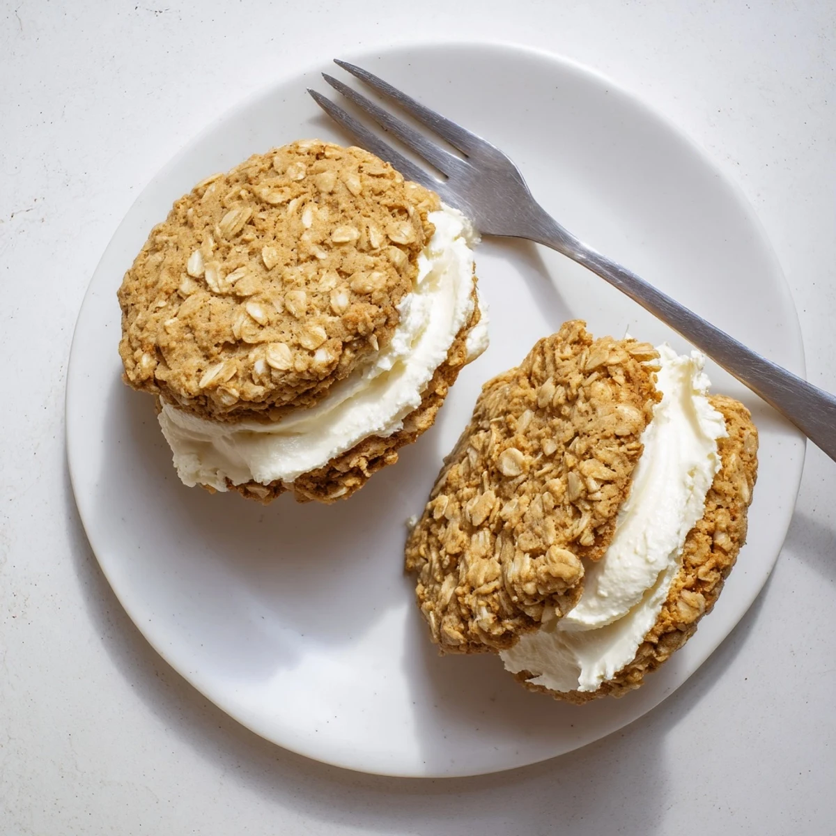 Freshly baked homemade oatmeal cream pies with sweet buttercream filling oozing from textured spiced oatmeal cookies