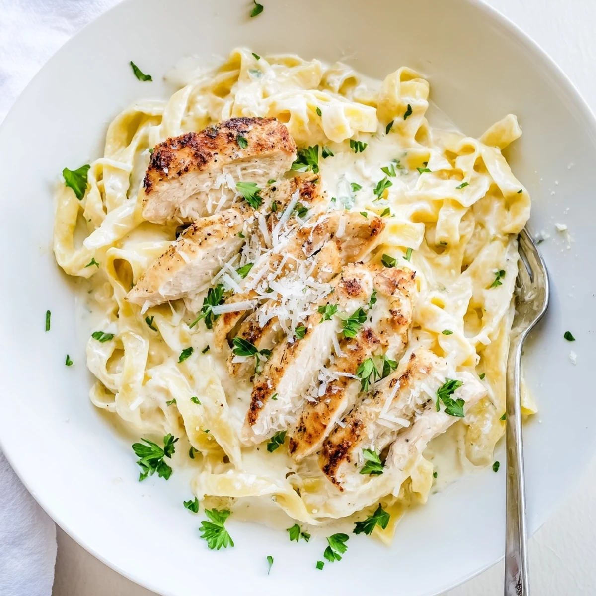 Steaming plate of chicken Alfredo pasta garnished with fresh parsley and extra cheese