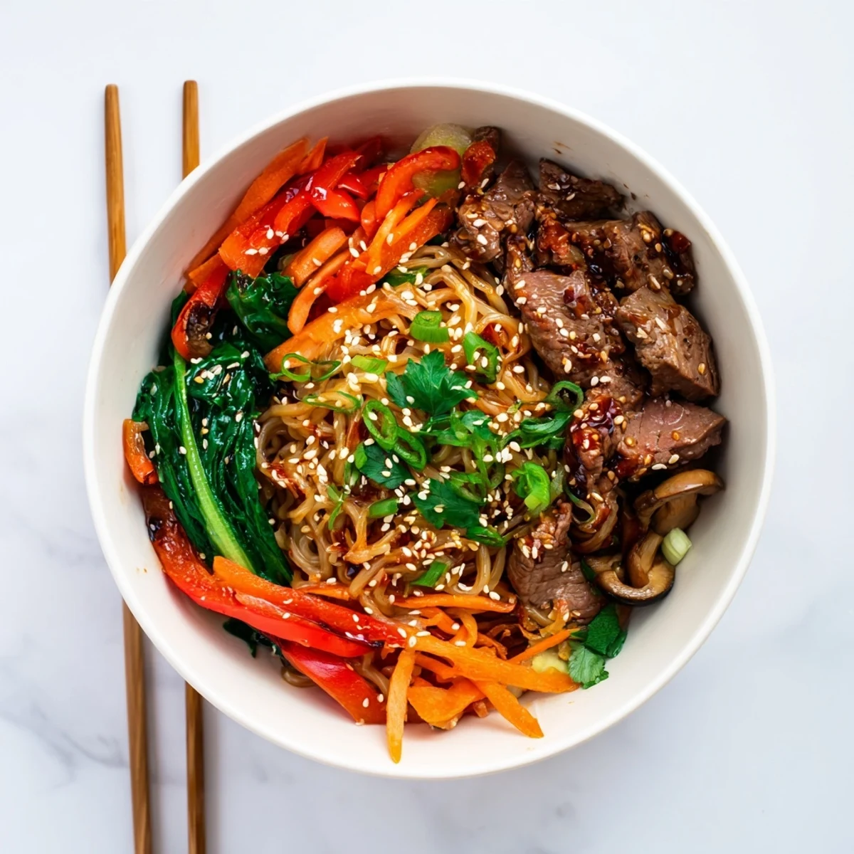 Close-up of Korean beef noodles dish with sesame-garnished beef, vibrant crisp vegetables, and spring potato noodles in rich chili glaze