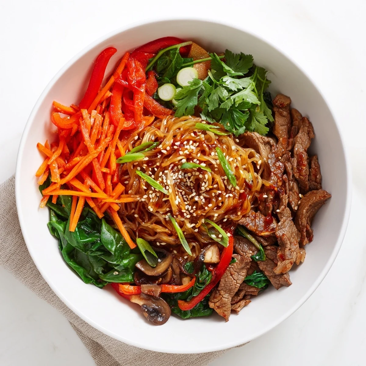 Plate of spicy Korean beef noodles featuring marinated beef, julienned carrots, bell peppers, and mushrooms tossed in glossy red sauce