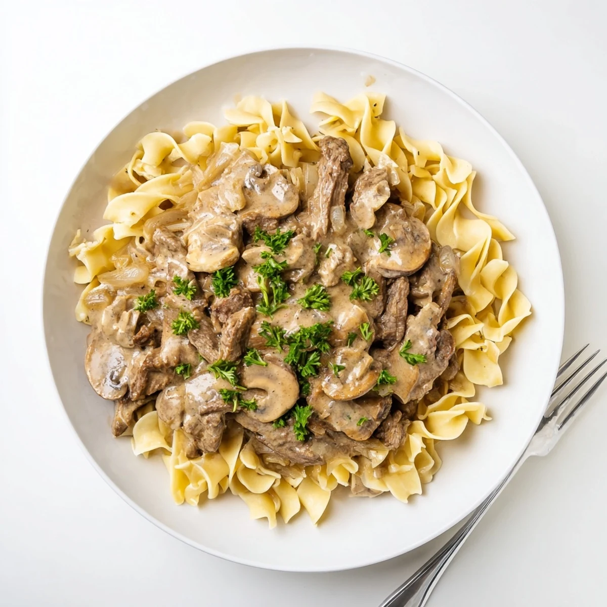 Creamy beef stroganoff served over egg noodles with fresh parsley garnish