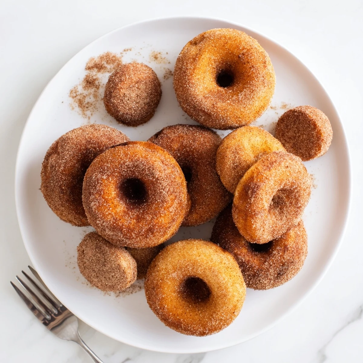 Warm homemade pumpkin spice donuts glistening with sugar coating beside a cup of coffee