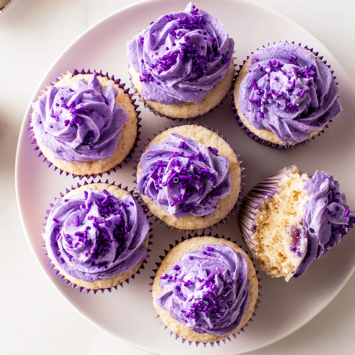 Fluffy purple grape soda cupcakes topped with smooth grape buttercream frosting on a white plate