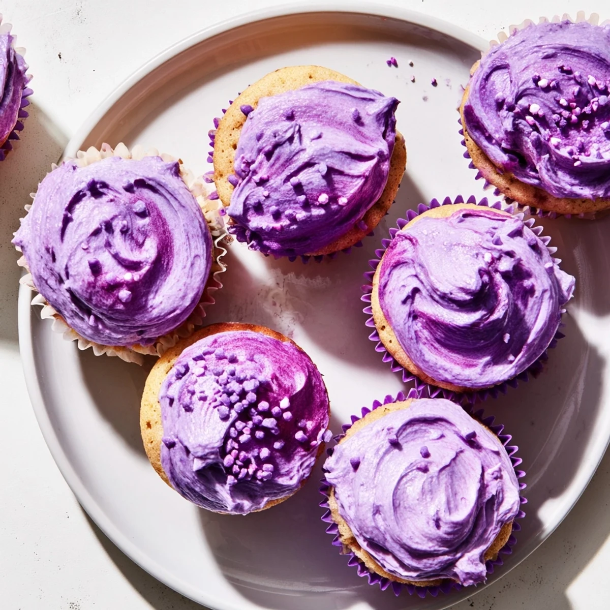 Golden grape soda cupcakes piped with grape buttercream and colorful garnishes on serving platter