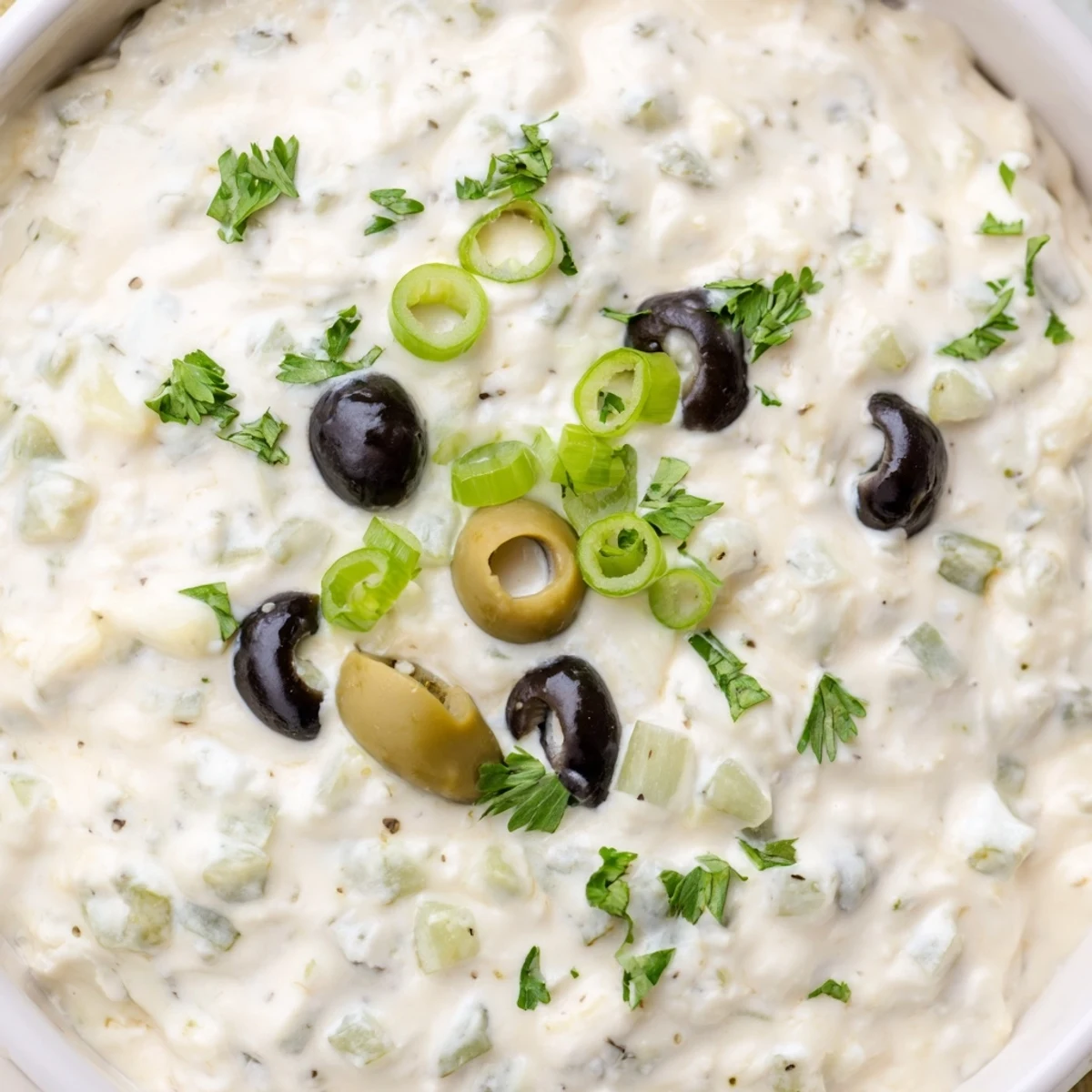Cream cheese olive dip served in a white bowl with crackers and fresh vegetable sticks