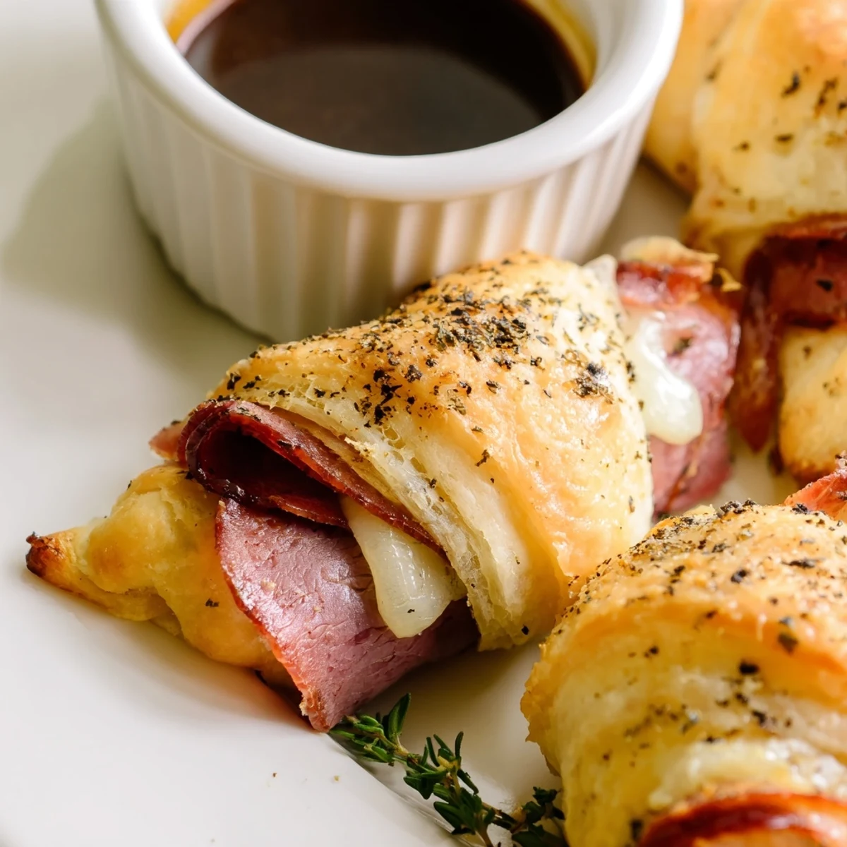 Golden beef and cheese French dip roll ups served with savory au jus dipping sauce on a rustic plate