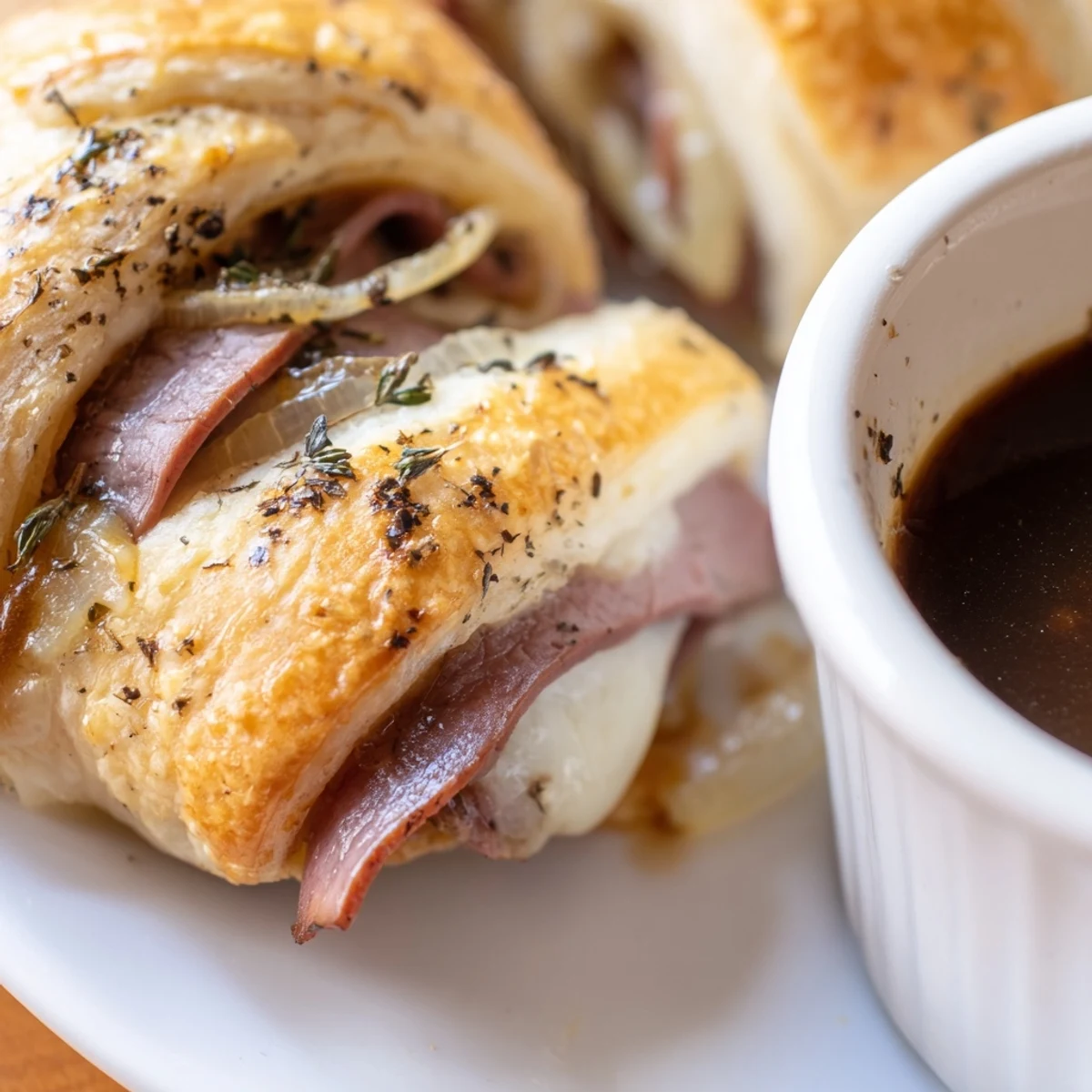 Crescent dough beef and cheese French dip roll ups bubbling with melted provolone beside warm broth