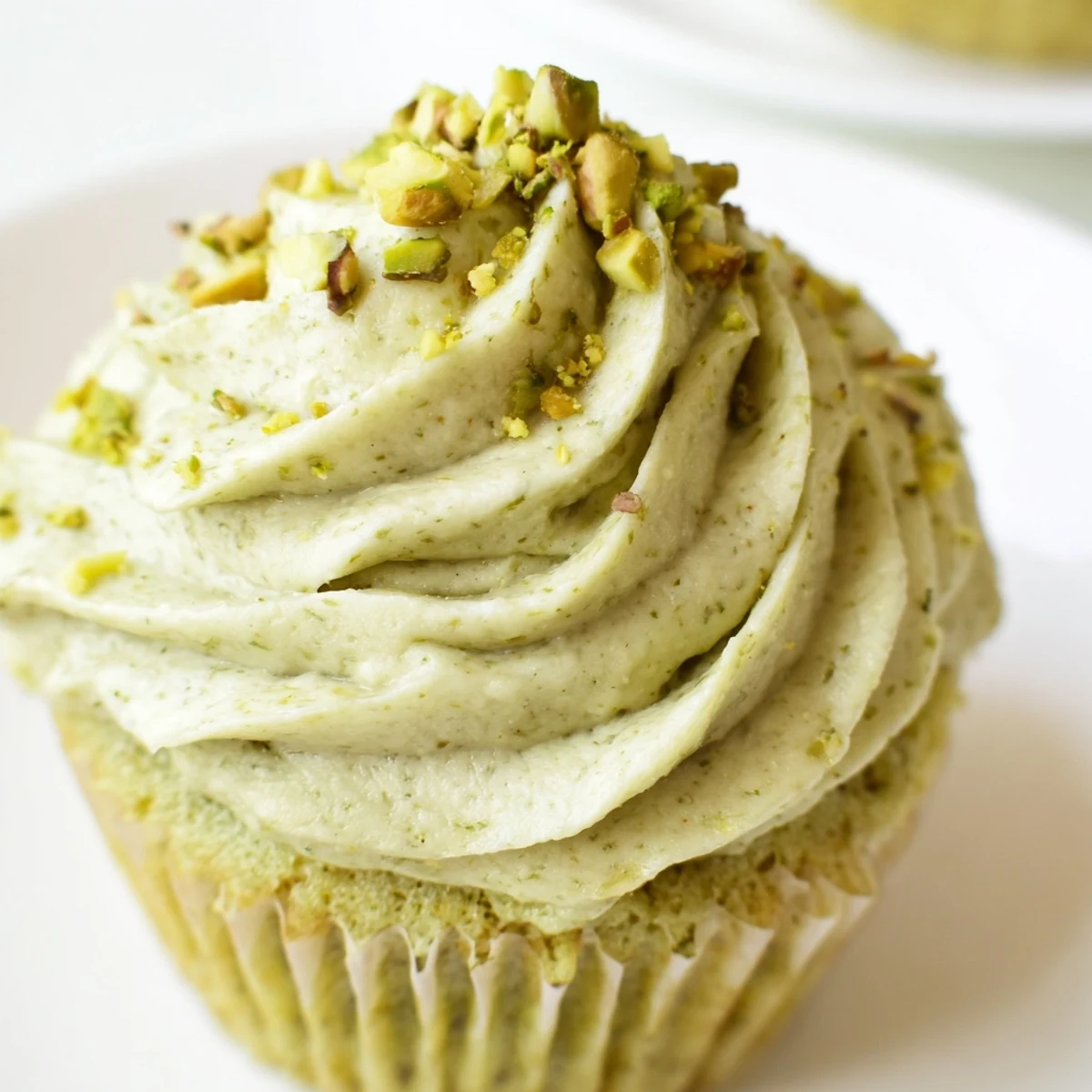 Pistachio cupcakes with swirled green buttercream topped with chopped pistachios on a rustic plate