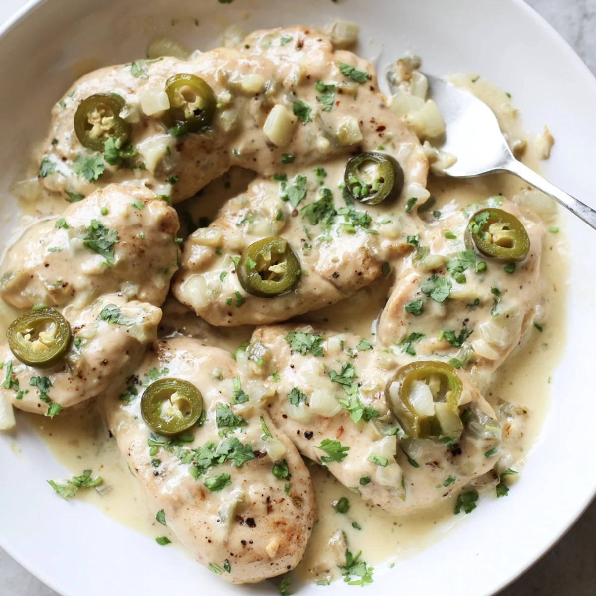 Golden jalapeno chicken breasts smothered in creamy white cheese sauce with fresh cilantro garnish