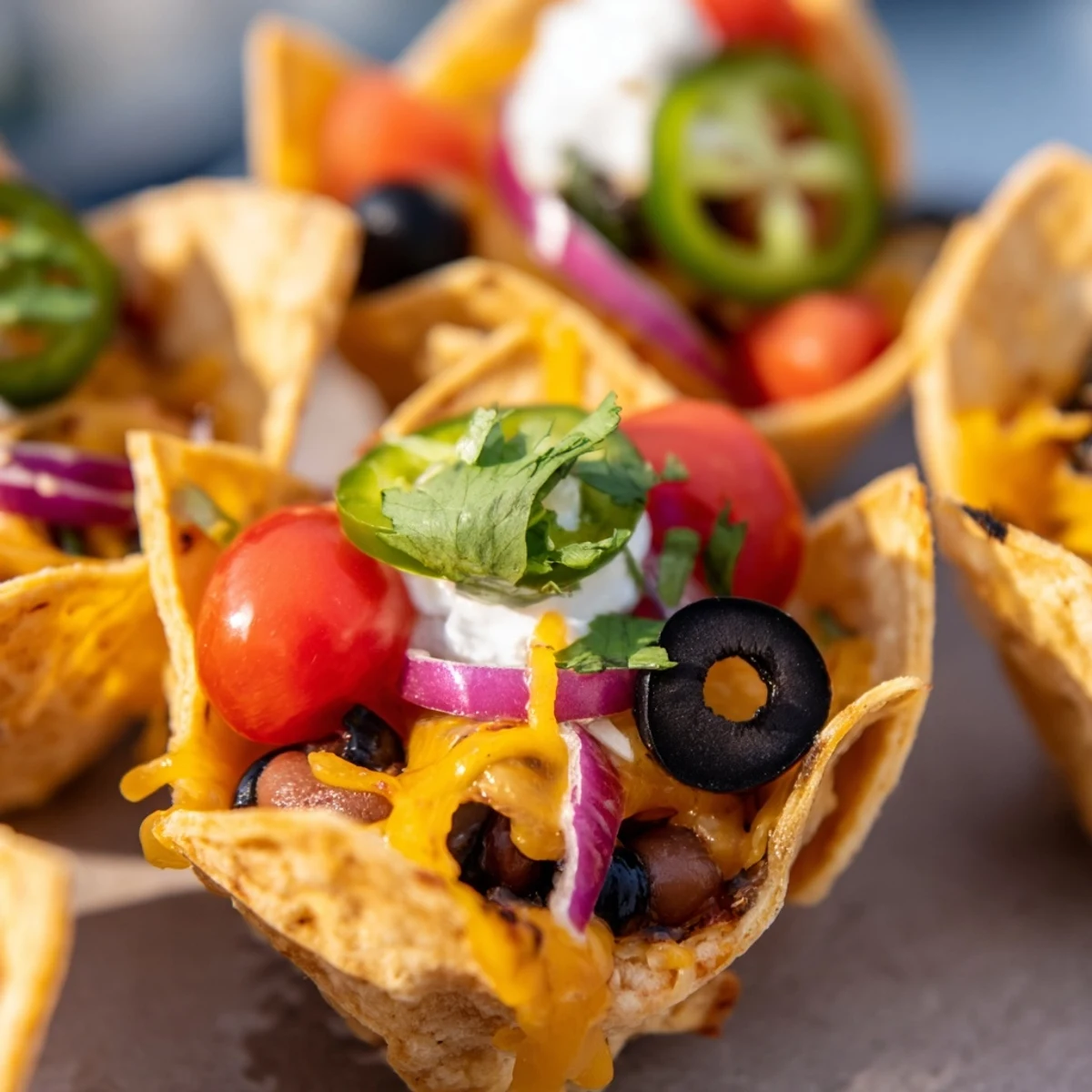 Golden cheesy nacho cups bubbling with melted cheddar and colorful fresh toppings in mini muffin tin