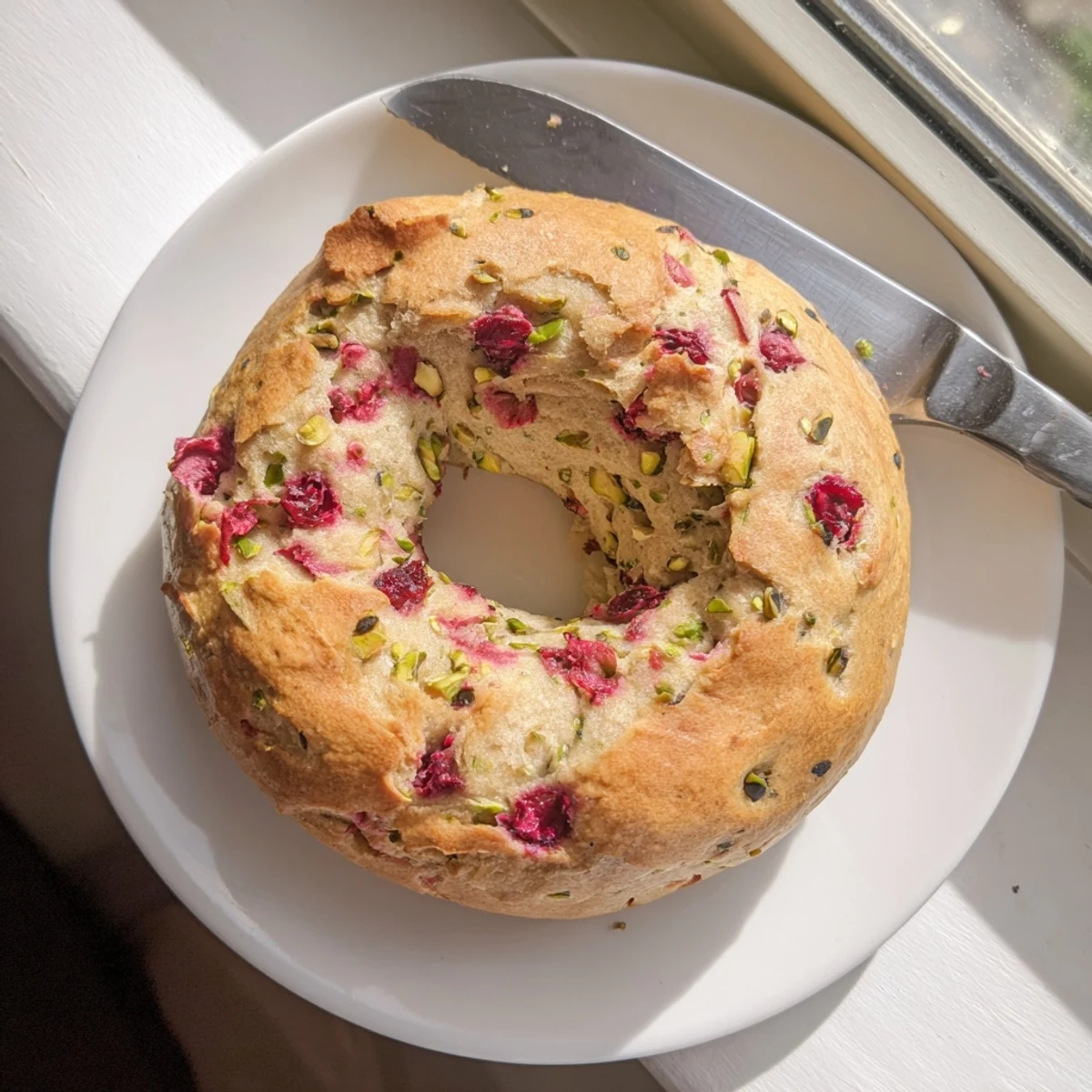 Golden brown raspberry pistachio sourdough bagels topped with crunchy nuts and ruby berry pieces