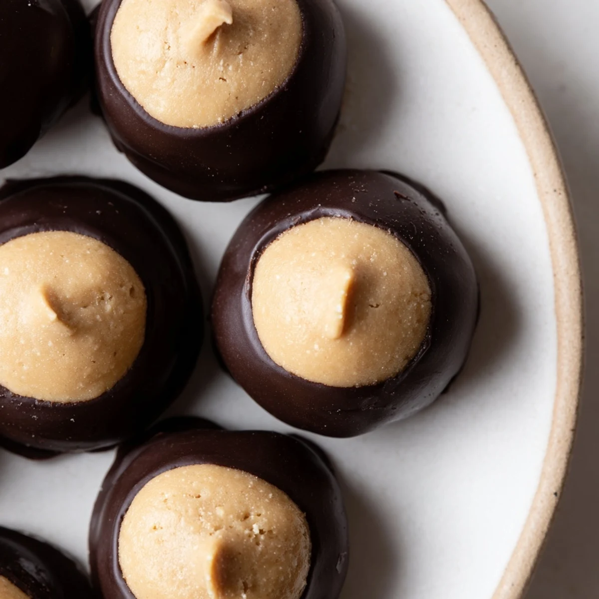 Chilled buckeye cookies arranged on parchment revealing smooth peanut butter tops above glossy chocolate