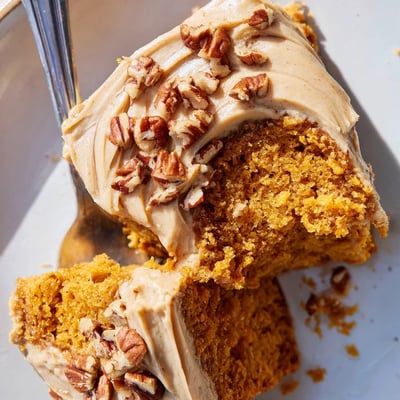 Warm pumpkin pecan cake topped with fluffy cinnamon cream cheese frosting and scattered toasted pecans