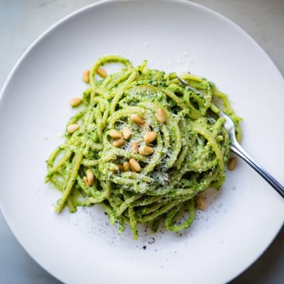 Bright green wild garlic pesto pasta coated in a silky, fragrant herb sauce on a white plate